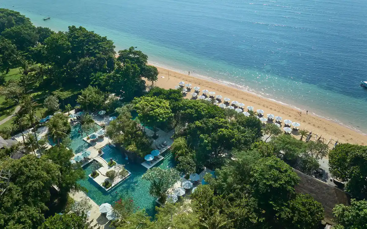 An aerial view of a beachfront resort, its pools and grounds meeting the sand