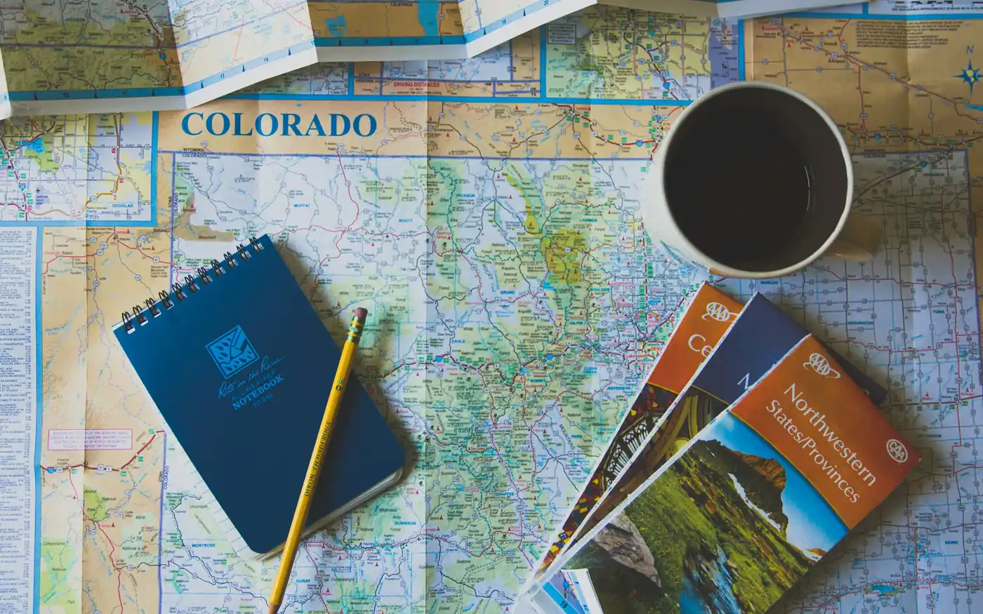 Route maps, a notebook and travel documents laid out for trip planning
