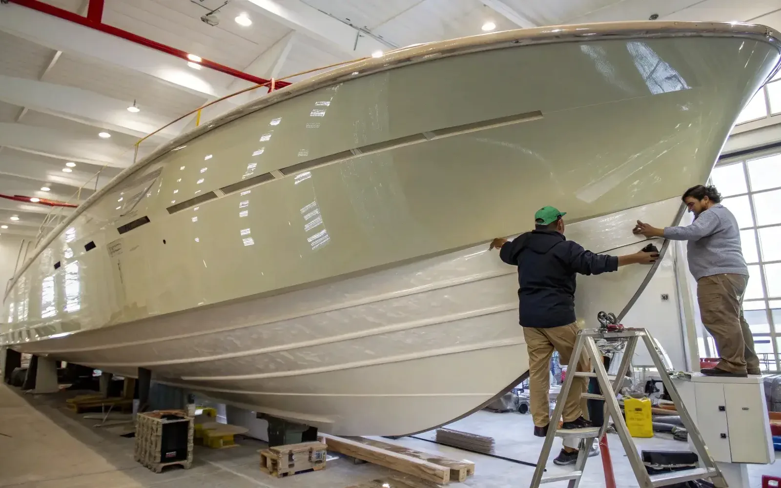 A vessel hull under construction in a covered boatyard, shipwrights working the topsides